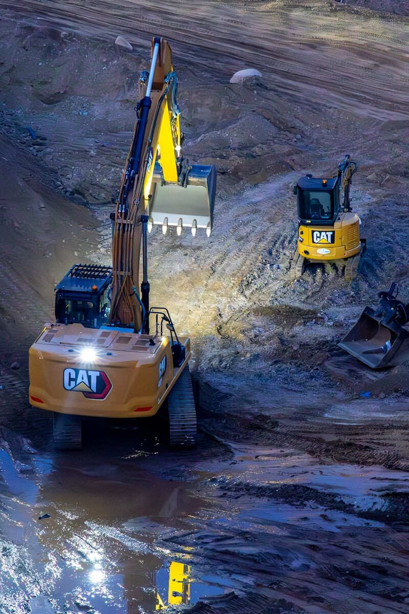 Two excavators working on a construction site at night.