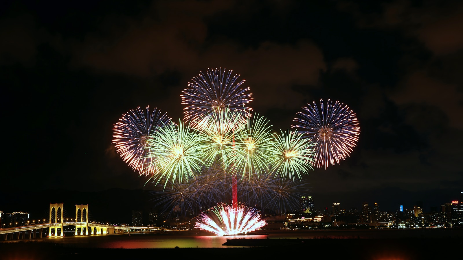 Colorful fireworks explode over a city skyline at night.