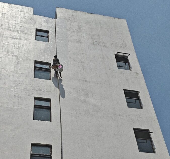 Worker rappels down building to wash windows.